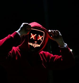 A spooky illuminated mask figure with a red hoodie in a dark setting, perfect for Halloween themes.