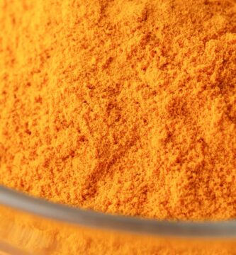 Close-up of bright turmeric powder in a glass bowl on an orange background, highlighting vibrant color contrast.